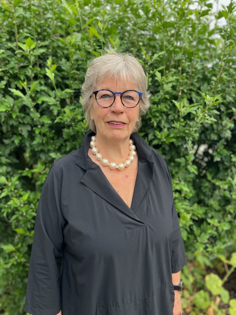 Trauerrednerin Beate Berdel-Mantz, lächelnd, in dunkler Kleidung vor einer grünen Hecke.